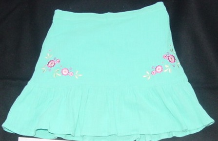 A WOVEN  CRINKLE COTTON SKIRT FOR GIRLS. WITH A HALF ELASTICATED WAIST
BAND. WITH A FRILL TO LOWER HALF. FLORAL EMBROIDERY TO FRONT. HEMMED A
T BASE OF GARMENT. HALF LINED.