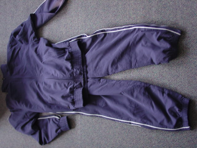 A WOVEN TRACK SUIT FOR UNISEX. LINED. A TWO-PIECE SET OF GARMENTS CONSISTING OF A JACKET DESIGNED TO COVER THE UPPER PART OF THE BODY FROM THE SHOULDERS TO THE HIPS WITH A COMPLETE FRONT OPENING FASTENED WITH A ZIP THAT EXTENDS UP INTO THE COLLAR. WITH LONG SLEEVES WITH ELASTICATED CUFFS. WITH TWO ZIPPED POCKETS. WITH ELASTICATION AT THE BASE OF THE GARMENT. WITH PIPING ON THE SLEEVES IN A CONTRASTING COLOUR. THE TROUSERS ARE DESIGNED TO COVER THE LOWER PART OF THE BODY FROM THE WAIST TO THE ANKLE ENVELOPING EACH LEG SEPARATELY. WITH AN ELASTICATED WAISTBAND WITH  DRAWSTRING TIGHTENING. WITH TWO SIDE ZIPPED POCKETS. WITH ELASTICATION AND ZIPS AT THE LEG ENDS.  WITH PIPING RUNNING DOWN EACH LEG IN A CONTRASTING COLOUR. LINED. 100% POLYESTER. PACKAGED TOGETHER IN A POLY BAG.