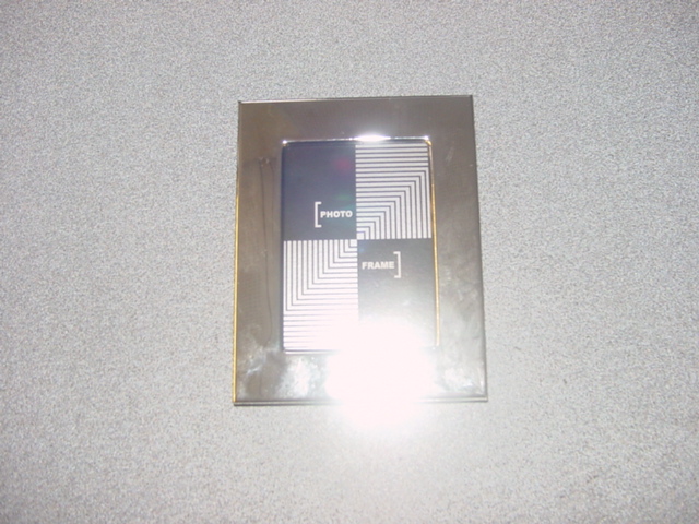 PHOTO FRAME. SILVER PLATED ON A BASE METAL. APPROXIMATELY 12CM LONG AND 9.5CM WIDE. PACKAGED TOGETHER IN SPECIFICALLY DESIGNED PACKAGING FOR RETAIL SALE AS A SET. WITH A BOOK THAT HAS BEEN CLASSIFIED SEPARATELY.