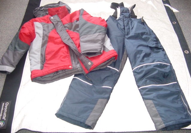 A WOVEN SKI SUIT FOR BOYS.  COMPRISING OF AN ANORAK AND SALOPETTES. PADDED AND LINED. ANORAK HAS A COMPLETE OPENING WITH A ZIP FASTENER AND A LEFT OVER RIGHT VELCRO AND POPPER CLOSURE.  WITH A FOLD AWAY ELASTICATED HOOD WITH VELCRO FASTENING. WITH A COLLAR. WITH LONG SLEEVES, WITH VELCRO TIGHTENING AT SLEEVE ENDS. WITH INNER RIBBED CUFFS.  WITH A ZIPPED POCKET EACH SIDE ON LOWER FRONT AND AN INSIDE BREAST POCKET. HEMMED AT BASE.  IN  CONTRASTING COLOURED FABRICS.  MATCHING TWO TONE PADDED SALOPETTES WITH PIPING. WITH A ZIP FLY WITH A LEFT OVER RIGHT POPPER CLOSURE.  ELASTICATED AT WAIST.  WITH BIB AT FRONT.  WITH  ADJUSTABLE ELASTICATED BRACES.  WITH ZIP AND VELCRO POCKETS. HEMMED AT LEG ENDS.  WITH A ZIPPED VENT AND  AN INNER ELASTICATED  CUFF.   100% POLYAMID.  WITH A COATING WHICH IS NOT DEEMED TO BE VISIBLE TO THE NAKED EYE.