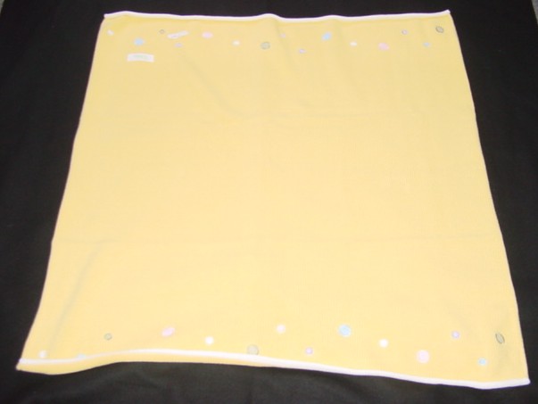 A KNITTED BLANKET FOR A BABY  MEASURING 83 X 91 CMS.  APPROX.  WITH BINDING ON TWO SIDES. WITH A CONTRASTING COLOURED BAND ON THE OTHER TWO SIDES  WITH A BORDER OF DIFFERENT SIZED COLOURED FABRIC CIRCLES ABOVE. PACKAGED IN A CARDBOARD BOX FOR RETAIL SALE.