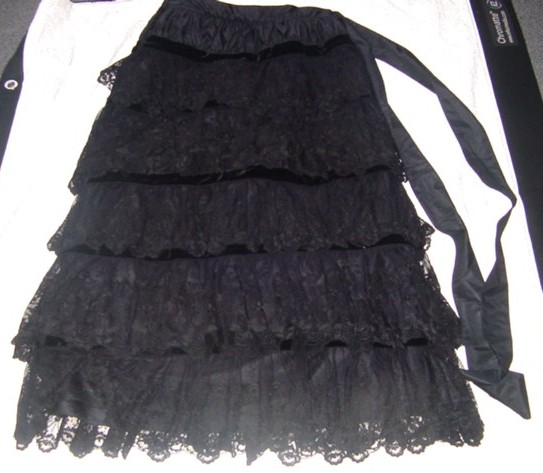 A WOVEN LONG SKIRT FOR WOMEN.  DESIGNED TO COVER THE LOWER PART OF THE BODY FROM THE WAIST TO THE ANKLES.  WITH AN ATTACHED WAISTBAND WITH A DECORATIVE TIE FASTENING.  WITH A PARTIAL OPENING ON THE LEFT HAND SIDE WITH A ZIP  AND HOOK AND EYE FASTENING.  MADE FROM  HORIZONTAL PANELS COVERED WITH LAYERS OF LACE EFFECT MATERIAL HELD IN PLACE BY STRIPS OF VELVET.  MAIN PART OF SKIRT IS 100% SILK.