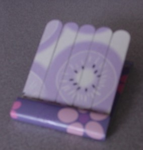 AN EMERY NAIL BOARD. AN ABRASIVE ON A BASE OF PAPERBOARD. MEASURING APPROXIMATELY 6.5CM LONG AND 5CM WIDE. FOR MANICURE PURPOSES.FIXED IN A CARDBOARD INSERT FOR DECORATION. PACKAGED WITH NAIL VARNISH, TOE SEPARATORS AND BUFFER BOARD WHICH HAVE ALL BEEN CLASSIFIED SEPARATELY.