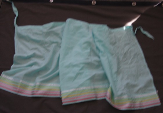 WOVEN WRAP AROUND SKIRT FOR WOMEN. INTENDED TO COVER THE LOWER PART OF THE BODY FROM THE WAIST TO THE KNEE. WITH SINGLE TIE FASTENING AT THE WAIST. BLUE IN COLOUR WITH COLOURED RIBBON AT BASE. HEMMED AT ALL EDGES. OF 100% COTTON.
