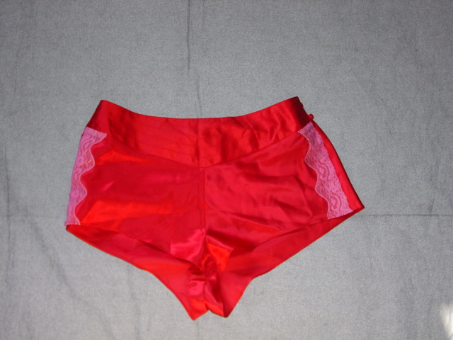 A PAIR OF WOVEN SHORTS STYLE BRIEFS FOR LADIES. WITH A N ELASTICATED WAIST. WITH A DECORATIVE PANEL TO FRONT, WITH TWO BUTTON FASTENING TO LEFT OF WAIST. WITH LACE TRIM TO SIDE SEAMS. HEMMED AT LEG ENDS. WITH A LINED GUSSET. 100% POLYESTER SATIN.