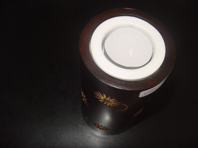 A WOODEN TEA LIGHT HOLDER. WITH A CIRCULAR CERAMIC INSERT TO HOLD THE TEA LIGHT. APPROX 150 MM HIGH AND 75 MM IN DIAMETER. WITH A CARVED DAISY PATTERN ON THE OUTER SURFACE.  HAND MADE.