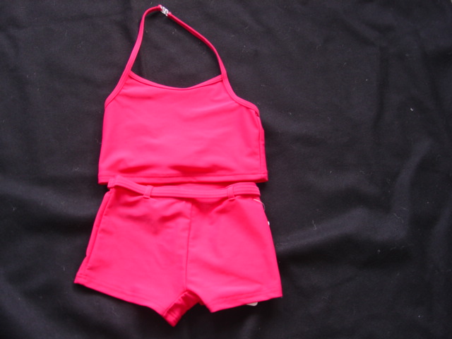 A KNITTED ENSEMBLE FOR GIRLS COMPRISING OF UPPER GARMENT.(a) A HALTER NECK BLOUSE DESIGNED TO COVER THE UPPER PART OF THE BODY TO THE WAIST. WITH FASTENING AT THE BACK OF THE NECK WITH A PLASTIC CLASP.(b) A PAIR OF SHORTS DESIGNED TO COVER THE LOWER PART OF THE BODY TO THE TOP OF THE THIGH. WITH A LINED GUSSET. WITH BELT LOOPS AND FABRIC THREADED THROUGH THE LOOPS TO FORM A MOCK BELT. GARMENTS  ARE PACKAGED ATTACHED TOGETHER AND ARE MADE OF A SINGLE IDENTICAL FABRIC. 80% POLYAMIDE, 20% ELASTANE