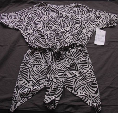A LADIES WOVEN BLOUSE WITHOUT OPENING FOR LADIES. DESIGNED TO COVER THE UPPER PART OF THE BODY TO THE TOP OF THE THIGH. WITH WIDE STRAIGHT NECKLINE AND RAGLAN SHORT SLEEVES. WITH ELASTICATED WAIST WHICH GIVES THE GARMENT A BLOUSON EFFECT. WITH TIE BELT ATTACHED WITH KEEPERS. FIXED WRAP OVER PANELSTO FRONT AND BACK OF GARMENT WHICH FINISH IN POINTS TO MID THIGH AT THE SIDES. 100% SILK