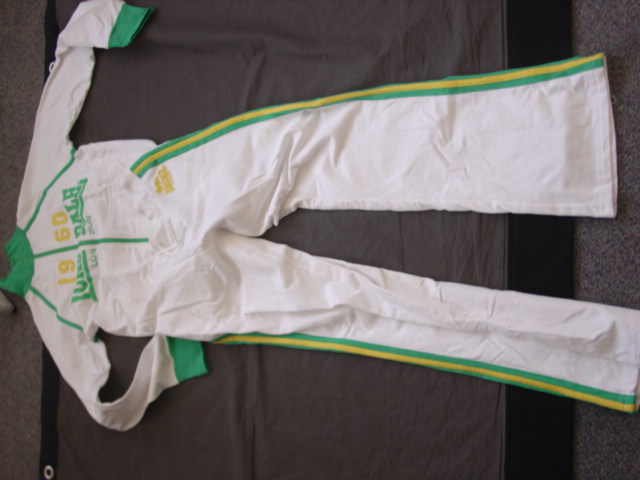 A KNITTED TRACK SUIT. CONSISTING OF AN UPPER AND LOWER GARMENT. THE UPPER GARMENT HAS A COMPLETE OPENING FASTENED WITH A ZIP THATS EXTENDS UP INTO THE COLLAR. WITH LONG SLEEVES. WITH RIBBING AT THE COLLAR SLEEVE ENDS AND BASE OF GARMENT ALL IN A CONTRASTING COLOUR. WITH A PRINTED LOGO ON THE FRONT AND BACK OF THE GARMENT. WITH FRONT POUCH POCKETS. THE LOWER CONSISTS OF A PAIR OF TROUSERS WHICH ENVELOPE EACH LEG SEPARATELY. WITH AN ELASTICATED RIBBED WAISTBAND WITH DRAWSTRING. WITH STRIPES IN CONTRASTING FABRIC ON THE SIDES OF EACH LEG. HEMMED AT LEG ENDS. 100% COTTON.