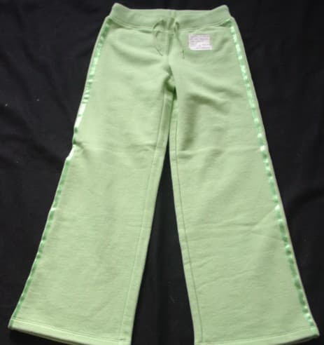 A PAIR OF KNITTED UNISEX TROUSERS FOR CHILDREN.  DESIGNED TO COVER THE LOWER PART OF THE BODY FROM THE WAIST TO THE ANKLES ENVELOPING EACH LEG SEPARATELY.  WITH AN APPLIED RIBBED WAISTBAND WITH A DRAWSTRING TIE.  WITH TWO NARROW BANDS OF RIBBON DOWN THE OUTSIDE OF EACH LEG.  WITH A BACK POCKET EACH SIDE WITH A FLAP AND BUTTON FASTENING WITH RIBBON DECORATION.  HEMMED AT LEG ENDS.  100% COTTON.