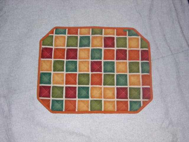 TABLE MAT (PLACE MAT) OF WOVEN COTTON. WITH PADDING OF MIXED FIBRES. MADE OF TWO CONTRASTING COLOURS. WITH PRINTEDTEXT. BOUND AT THE EDGES. APPROX MEASUREMENTS: 44.5 X 34.5 CM.