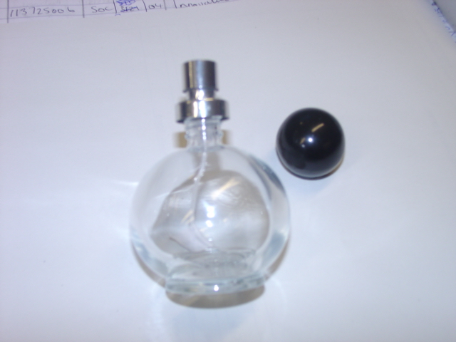 A GLASS SCENT BOTTLE. WITH ATOMISER SPRAY.  WITH BLACK PLASTIC LID. APPROX 8CMS HIGH. PACKAGED IN A CIRCULAR CARDBOARD BOX.