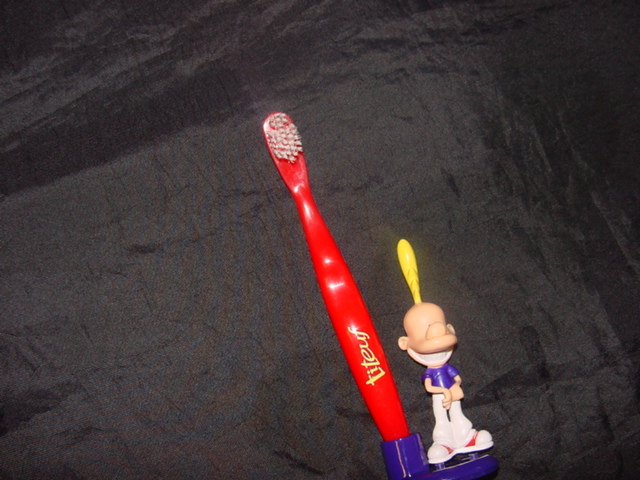 A CHILDS TOOTHBRUSH AND TOOTHBRUSH STAND WITH A SMALL PLASTIC FIGURE ATTACHED TO THE BASE. PACKAGED TOGETHER FOR RETAILS SALE IN A BLISTER PACK WITH CARDBOARD BACKING.
