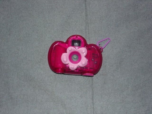 A CHILD 35MM PHOTOGRAPHIC CAMERA. MADE OF PLASTIC WITH A FLOWER DESIGN AT THE LENS. WITH FILM WINDER. WITH PLASTIC CLIP FOR CARRYING. PACKAGED IN A BAG AS A SET WITH BANDANA AND BODY SPRAY, CLASSIFIED SEPARATELY.