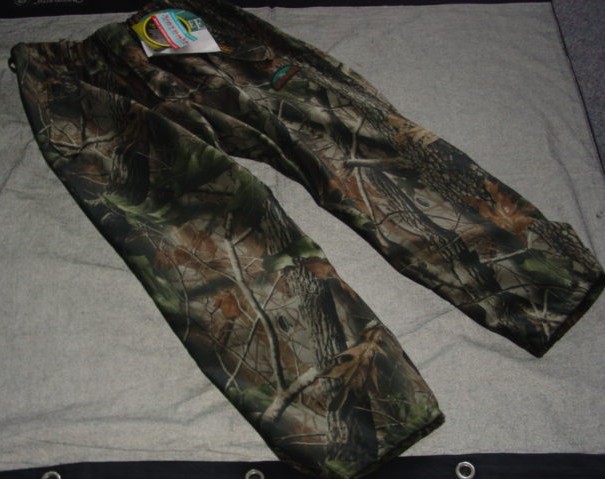 A PAIR OF KNITTED CAMOUFLAGE PRINT TROUSERS FOR MEN.  DESIGNED TO COVER THE LOWER PART OF THE BODY FROM THE WAIST TO THE ANKLE, ENVELOPING EACH LEG SEPARATELY.   LINED.   WITH AN ELASTICATED WAIST WITH BELT LOOPS.  WITH A LEFT OVER RIGHT FLY FASTENING.  WITH A DIAGONAL ZIPPED POCKET WITH FLAP EACH SIDE AT FRONT.  HEMMED AT LEG ENDS.  WITH POPPER ADJUSTMENT AT LEG ENDS.  WITH LOGOS.  BRUSHED FABRIC, WITH A WATERPROOF MEMBRANE  ON THE INNER SURFACE WHICH IS NOT DEEMED TO BE VISIBLE TO THE NAKED EYE. 100% POLYESTER.