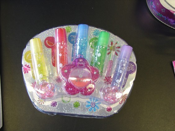 Childrens Lip Gloss Set.  Consists of  five lip glitters (kissing fruit gloss),  Two lip gloss in flower shaped pl;astic container, small brush, and two plastic flower shaped hair clips.  The items are put up for retail sale packed inside a plastic case complete with plastic handle and lock. The plastic case has been classified separately.
