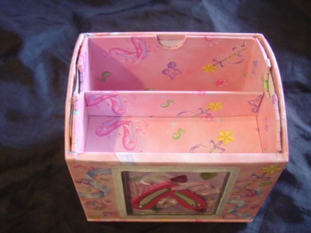 A SQUARE SHAPED BOARD CONTAINER ON A SPINNING BASE DECORATED WITH GLITTER, RIBBON, RHINESTONE JEWELS AND PLASTIC SHAPED SHOES, DISPLAYED BENEATH A CELLOPHANE WINDOW. PHOTOGRAPHS CAN BE INSERTED IN SIDE PANELS ON EITHER SIDE OF THE CONTAINER. THE CONTENTS OF THE BOX HAVE BEEN CLASSIFIED SEPARATELY.