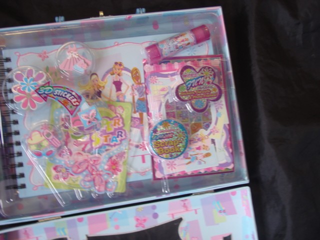 A RECTANGULAR CARRY CASE MADE FROM BOARD WITH A PLASTIC HANDLE, METAL CATCH AND HINGES DECORATED WITH GLITTER. THE CASE CONTAINS A SCRAPBOOK, GLUE, FOUR GEL PENS, ROLLER STAMPER ON A KEY CHAIN, A SHEET OF STICKERS, SIX DIE CUT FRAMES, 3D STICKERS AND SIX CUT OUT SHAPES. THE ESSENTIAL CHARACTER OF THE SET IS GIVEN BY THE SCRAPBOOK.