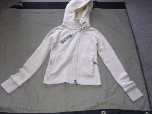A GARTER STITCH KNITTED WIND-JACKET FOR UNISEX. SIMILAR TO A CARDIGAN. WITH LONG SLEEVES.  WITH A DEEP RIBBING TO BASE OF GARMENT AND SLEEVE ENDS. WITH ZIP POCKETS TO LOWER FRONTS. WITH A COMPLETE OPENING WITH A ZIP FASTENER. WITH A HOOD WITH AN EMRBOIDERED LOGO, AND A LINING OF PILE FABRIC. OF WOOL.