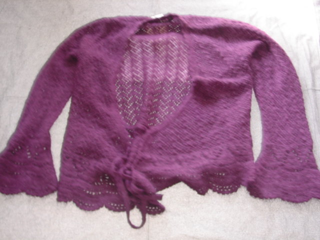 A KNITTED WRAP OVER CARDIGAN FOR WOMEN. DESIGNED TO COVER THE UPPER PART OF THE BODY FROM THE SHOULDERS TO THE HIPS. WITH LONG SLEEVES WIDENING AT THE CUFFS. WITH A V-NECKLINE. WITH TWO TIE WRAP OVER FASTENINGS. WITH A SCALLOPED EACH AT THE BASE OF THE GARMENT. 100% MOHAIR.