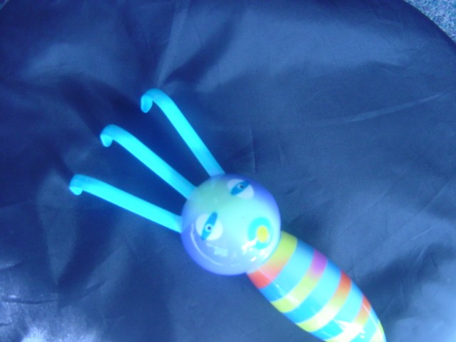 A SMALL HAND HELD GARDEN FORK. THE FORK HAS A HANDLE OF A BRIGHTLY COLOURED INSECT AND HAS THREE METAL PRONGS. PACKAGED FOR RETAIL SALE IN A CLEAR CONTAINER.
