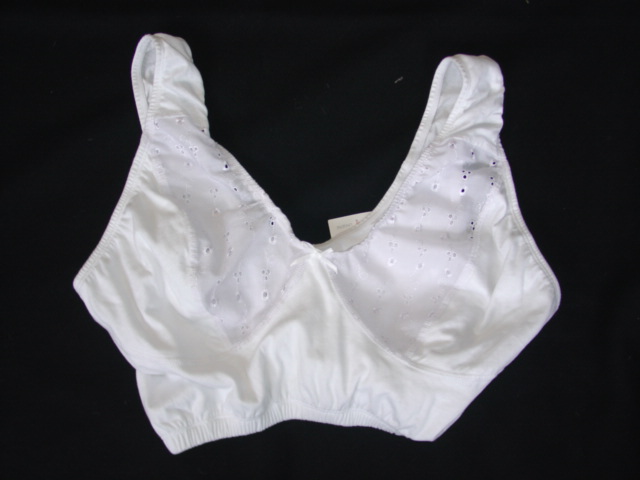 A KNITTED CROPPED LIGHTWEIGHT UNDERGARMENT, SIMILAR TO A BRA.  WITH SHAPED, SEAMED CUPS, THE UPPER HALF OF THE CUPS ARE OF WOVEN BRODERIE ANGLAIS FABRIC. NOT CONSIDERED TO BODY SUPPORTING. ELASTICATED AROUND ARMHOLES AND AT BASE OF GARMENT.  WITH DECORATIVE BOW AT FRONT.  WITH BROAD NON-ADJUSTABLE SHOULDER STRAPS.  95% COTTON AND 5% POLYESTER
