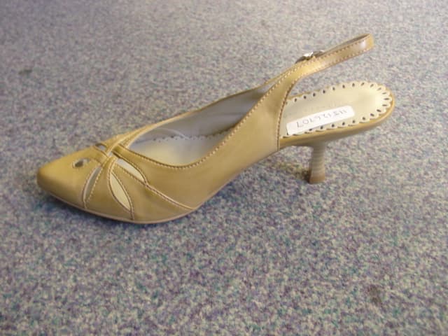 LADIES HIGH HEELED FASHION SHOE. NOT COVERING THE ANKLE.  UPPERS OF PLASTIC.  BACKLESS WITH A STRAP AROUND THE BACK OF THE ANKLE.OUTER SOLE OF PLASTIC. ORNAMENTAL CUT OUT DECORATION ON THE FRONT. WITH POINTED TOE. HEEL MEASURES APPROXIMATELY 5.5cm IN HEIGHT. INSOLE LENGTH EXCEEDING 24 cm. BEIGE IN COLOUR.