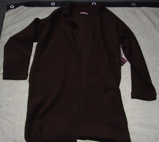 A KNITTED COAT FOR UNISEX.  UNLINED.  DESIGNED TO COVER THE BODY FROM THE SHOULDERS TO BELOW THE KNEE.  WITH A COMPLETE OPENING WITHOUT FASTENING.  WITH A REVER COLLAR.  WITH LONG SLEEVES WITH TURN BACK CUFFS.  WITH A PATCH POCKET EACH SIDE AT HIP LEVEL.  OVERLOCKED AT EDGES.  WITH DECORATIVE STITCHING AROUND COLLAR, DOWN EACH SIDE OF FRONT, BASE  AND AROUND CUFFS.  100 PERCENT WOOL.