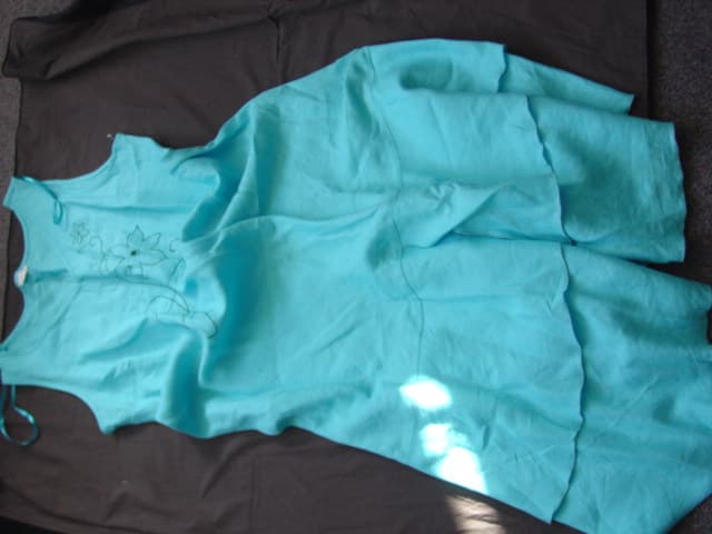 WOVEN DRESS FOR WOMEN.  REACHING DOWN TO BELOW THE KNEES.  V-NECK WITHOUT OPENING.  WITHOUT SLEEVES.  WITH APPLIED FRILL TOWARDS BASE.  EMBROIDERY ON FRILL AND BASE.  OVERSEWN AT BASE.  WITH EMBROIDERY ON FRONT.  100 PERCENT LINEN