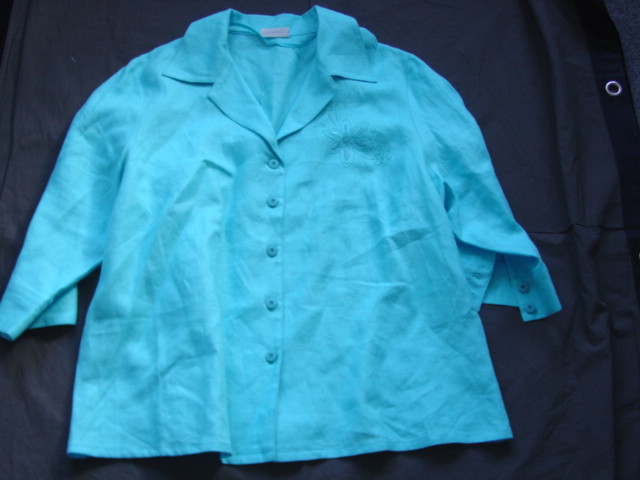 WOVEN BLOUSE FOR WOMEN.  REACHING DOWN TO BELOW THE WAIST.  V NECK WITH COLLAR.  COMPLETE FRONT OPENING FASTENED RIGHT OVER LEFT BY BUTTONS.  LONG SLEEVES WITH BUTTON CUFFS AT SLEEVE ENDS.  HEMMED AT BASE.  WITH EMBROIDERED DESIGN ON LEFT CHEST.  100 PERCENT LINEN