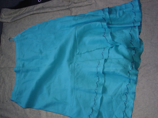 WOVEN SKIRT FOR WOMEN.  REACHING DOWN TO BELOW THE KNEE.  PARTIALLY ELASTICATED AT SIDES OF WAISTBAND WITH PARTIAL SIDE OPENING FASTENED BY ZIP AND SINGLE BUTTON.  OVERSEWN AT BASE.  WITH APPLIED FRILL TOWARDS BASE.  EMBROIDERY ON FRILL AND BASE.  100 PERCENT LINEN