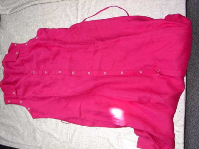 WOVEN DRESS FOR WOMEN. REACHING DOWN TO BELOW THE KNEE. V NECK WITH COLLAR.  COMPLETE FRONT OPENING FASTENED RIGHT OVER LEFT BY PRESS STUDS.  WITHOUT SLEEVES. BOUND AT ARMHOLES WITH DECORATIVE EYELET DETAIL.  HEMMED AT BASE.  WITH TIES EXTENDING FROM SIDE OF WAIST.  100 PERCENT LINEN