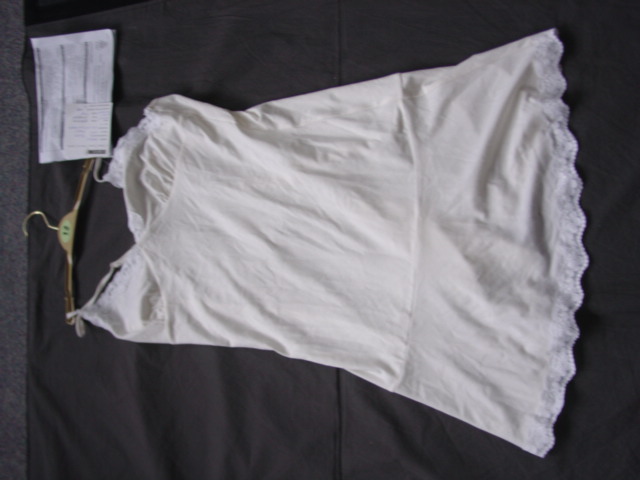 A KNITTED NIGHTDRESS FOR WOMEN. DESIGNED TO COVER THE UPPER PART OF THE BODY FROM THE SHOULDERS TO MID THIGH. WITH THIN ADJUSTABLE SHOULDER STRAPS. WITHOUT AN OPENING. WITH A V-NECKLINE. WITH AN A APPLIED FLUTED PIECE OF FABRIC AT THE BASE OF THE GARMENT. WITH APPLIED LACE AT THE NECKLINE AND AT THE BASE. OF MAN-MADE FIBRES. PACKAGED ON A HANGER.