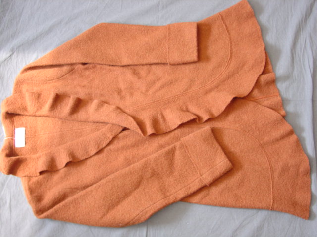 A WOMEN'S KNITTED FOUR PANELLED JACKET OF BOILED WOOL. WITH LONG SLEEVES WITH TURN-UP CUFFS. WITH WIDE FRILLED EDGING COMPLETELY AROUND THE GARMENT. WITH A TIE FASTENING UNDER THE BUST. INTENDED TO COVER THE BODY FROM THE SHOULDERS TO MID-THIGH. NOT LINED. WITHOUT POCKETS.