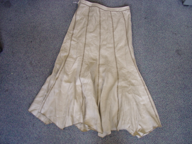WOMENS WOVEN SKIRT. REACHING DOWN TO BELOW THE KNEE. WITH PARTIAL OPENING AT THE BACK FASTENED BY A ZIP AND SINGLE BUTTON. WITH PANELS AND CONTRAST STITCHING. OVERLOCKED AT BASE OF GARMENT. OF LINEN.