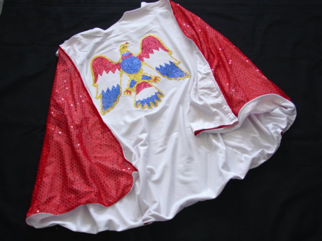 A KNITTED POLYESTER LINED CAPE FOR UNISEX. WITH A DECORATIVE EAGLE ON THE BACK COMPLETE WITH DIAMANTE AND METAL STUDS. WITH VELCRO TO ENABLE IT TO BE ATTACHED TO MATCHING PULLOVER.  IMPORTED AS PART OF AN ELVIS PRESLEY FANCY DRESS COSTUME PACKAGED TOGETHER IN A POLY BAG WITH A PLASTIC HOOK. WITH A PRINTED CARDBOARD INSERT.