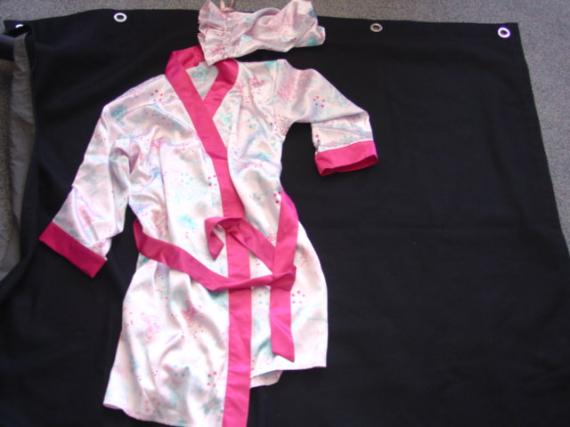 A WOVEN, PRINTED SATIN DRESSING GOWN FOR GIRLS. WRAP-OVER STYLE WITH A TIE BELT. ELASTICATED AT BACK OF WAIST. WITH LONG SLEEVES.BANDS, BELT, BELT LOOPS AND CUFFS ARE OF A CONTRASTING PLAIN FABRIC. HEMMED AT BASE OF GARMENT. OF POLYESTER. PACKAGED IN A DRAWSTSRING BAG OF THE SAME FABRIC.