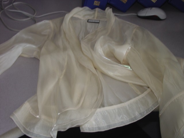 A LADIES WOVEN JACKET MADE OF 53% POLYESTER AND 47% NYLON. TWO HOOK AND EYE FASTENINGS. FRILL AROUND THE COLLAR AND ON THE ARMS. FALLS BELOW THE WAIST.
