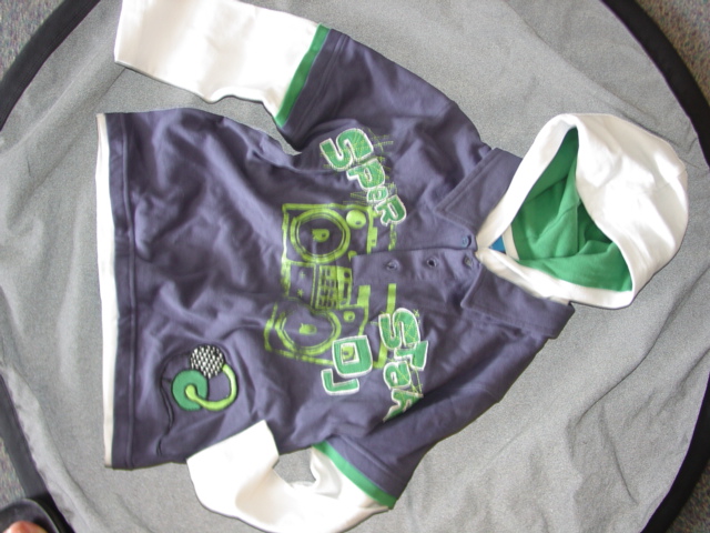 BOYS KNITTED PULLOVER WITH A HOOD. REACHING DOWN FROM THE NECK TO BELOW THE WAIST. WITH ATTACHED INNER TOP WITH ROUND NECK WITHOUT OPENING. WITH A COLLAR. WITH A NON FUNCTIONAL PARTIAL OPENING AT THE FRONT OF OUTER LAYER. WITH NON FUNCTIONAL BUTTON FASTENING LEFT OVER RIGHT. WITH LONG SLEEVES. HEMMED AT SLEEVE ENDS AND BASE OF GARMENT. WITH A PRINTED/SEWN ON DESIGN ACROSS THE FRONT OF THE CHEST. 100 PERCENT COTTON