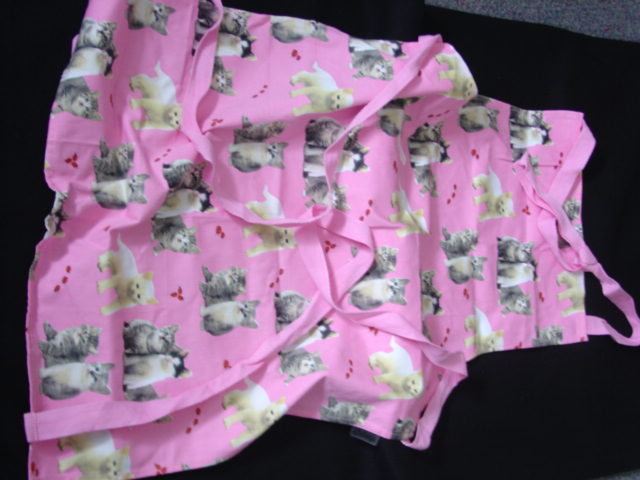 APRON MADE OF WOVEN COTTON TEXTILE.  WITH TIE FASTENING AROUND NECK AND AT WAIST. PINK IN COLOUR WITH CAT AND LADYBIRD PRINT DECORATION.  HEMMED. 100 PERCENT COTTON