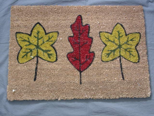 A TUFTED DOOR MAT OF COIR FIBRE WITH A PVC LATEX RUBBER BACKING.. WITH A PAINTED LEAF DESIGN.