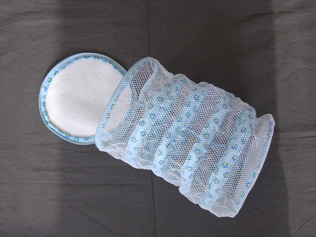 A WASHING BAG FOR TRAINERS MADE FROM KNITTED MESH NET FABRIC OF MAN-MADE TEXTILE.  A CIRCULAR SHAPE WITH FOAM RIBS KEEPING THE BAG IN SHAPE. MEASURING APPROXIMATELY 35 CM LONG AND 20 CM IN DIAMETER.  WITH A ZIP OPENING AROUND ONE END.  WITH A LOOP AT EITHER END TO ALLOW BAG TO BE HUNG ON WASHING LINE.