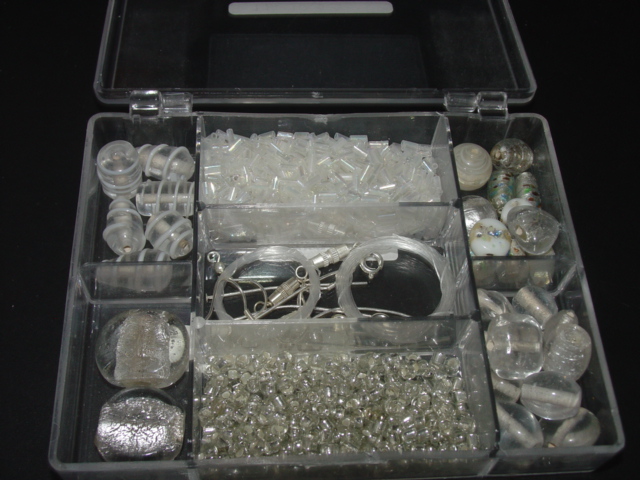 A PLASTIC BOX FILLED WITH VARIOUS SIZED AND SHAPED AND DECORATED GLASS BEADS. ALSO PACKAGED WITHIN THE BOX IS SOME PLASTIC STRING TO MAKE NECKLACES AND BASE METAL PARTS FOR MAKING EARRINGS WITH.