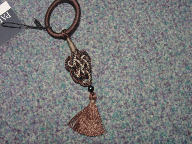 A NAPKIN RING. A PLASTIC RING COVERED WITH RAYON CORD. WITH A DECORATIVE TEXTILE TASSEL ATTACHED.