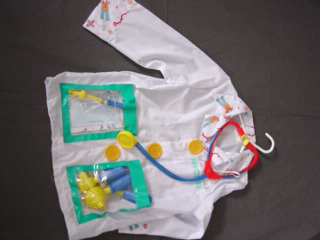 WOVEN JACKET FOR BOYS.  DOCTOR FANCY DRESS COSTUME.  WITH V-NECK.  WITH COLLAR.  COMPLETE FRONT OPENING FASTENED LEFT OVER RIGHT BY VELCRO WITH MOCK BUTTONS ON FRONT.  LONG SLEEVES.  WITH CUFFS.  HEMMED AT BASE. WITH ONE TEXTILE  CHEST POCKET AND TWO LOWER POCKETS OF CLEAR PLASTIC SHEETING.  84 PERCENT POLYESTER AND 16 PERCENT COTTON. PACKED IN A PLASTIC BAG WITH CARD INSERT AS A SET WITH ACCESSORIES CONSISTING OF A TEXTILE FACE MASK AND HAT, TOY PLASTIC STETHOSCOPE, SYRINGE AND MEDICAL TOOLS WITH PRESCRIPTION PAD.