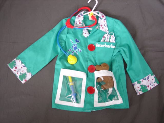 WOVEN JACKET FOR BOYS.  VETERINARIAN  FANCY DRESS COSTUME.  WITH V-NECK.  WITH COLLAR.  COMPLETE FRONT OPENING FASTENED LEFT OVER RIGHT BY VELCRO WITH MOCK BUTTONS ON FRONT.  LONG SLEEVES.  WITH CUFFS.  HEMMED AT BASE. WITH ONE TEXTILE  CHEST POCKET AND TWO LOWER POCKETS OF CLEAR PLASTIC SHEETING.  90 PERCENT POLYESTER AND 10 PERCENT COTTON. PACKED IN A PLASTIC BAG WITH CARD INSERT AS A SET WITH ACCESSORIES CONSISTING OF A TEXTILE FACE MASK, TOY PLASTIC STETHOSCOPE, SYRINGE AND SMALL POCKET SIZED PUPPY WITH BANDAGED LEG.