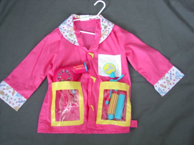 WOVEN JACKET FOR BOYS.  HAIRDRESSER FANCY DRESS COSTUME.  WITH V-NECK.  WITH COLLAR.  COMPLETE FRONT OPENING FASTENED LEFT OVER RIGHT BY VELCRO WITH MOCK NOVELTY BUTTONS ON FRONT.  LONG SLEEVES.  WITH CUFFS.  HEMMED AT BASE. WITH ONE COTTON CHEST POCKET AND TWO LOWER POCKETS OF CLEAR PLASTIC SHEETING.  90 PERCENT POLYESTER AND 10 PERCENT COTTON. PACKED IN A PLASTIC BAG WITH CARD INSERT AS A SET WITH ACCESSORIES CONSISTING OF A TOY MOCK PLASTIC HAIRDRYER, TONGS AND BRUSH.