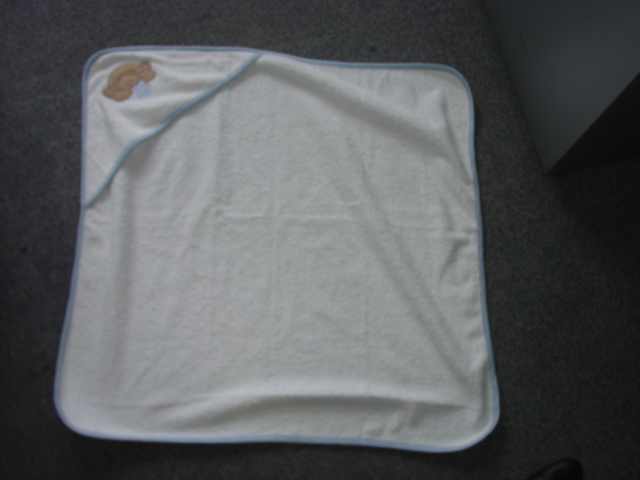 A KNITTED TOWEL. WITH AN APPLIED PIECE OF MATERIAL TO FORM A HOOD WITH AAPPLIED BEAR MOTIF. OF TERRY TOWELLING. FOR BABY. WITH APPLIED TRIM. OF 100 PER CENT COTTON. 74CM x 77CMS APPROX