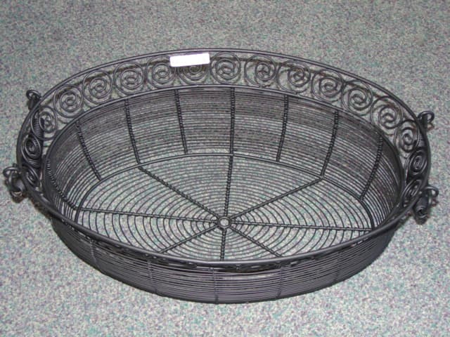 LARGE OVAL WIRE BASKET MADE OF IRON AND PAINTED BLACK. DECORATED WITH SPIRALS AROUND THE TOP. WITH CARRY HANDLES. PART OF A SPA SET IN AN IRON WIRE BASKET, THE OTHER PARTS OF WHICH HAVE ALL BEEN CLASSIFIED SEPARATELY.
