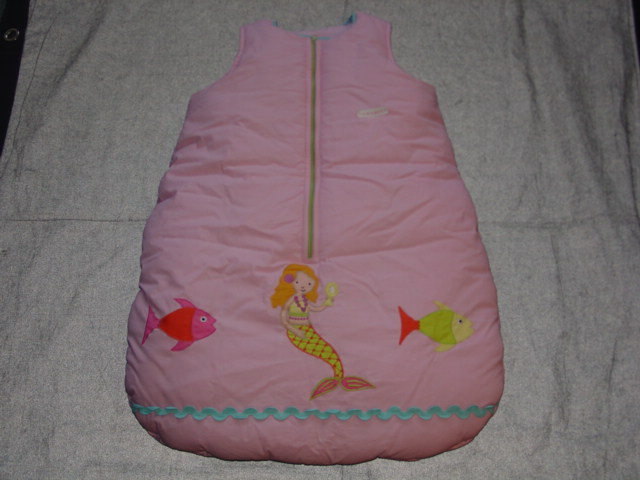 A BABIES PADDED SLEEPING BAG DESIGNED TO BE WORN BY THE BABY. WITH ROUND NECK AND ARMHOLES. WITH ZIP FASTENING DOWN CENTRE FRONT. WITH APPLIQUE AND EMBROIDERED DESIGN TO FRONT BASE OF GARMENT. LENGTH APPROX 71 CMS. 100 PER CENT COTTON FILLED WITH A COTTON WADDING.